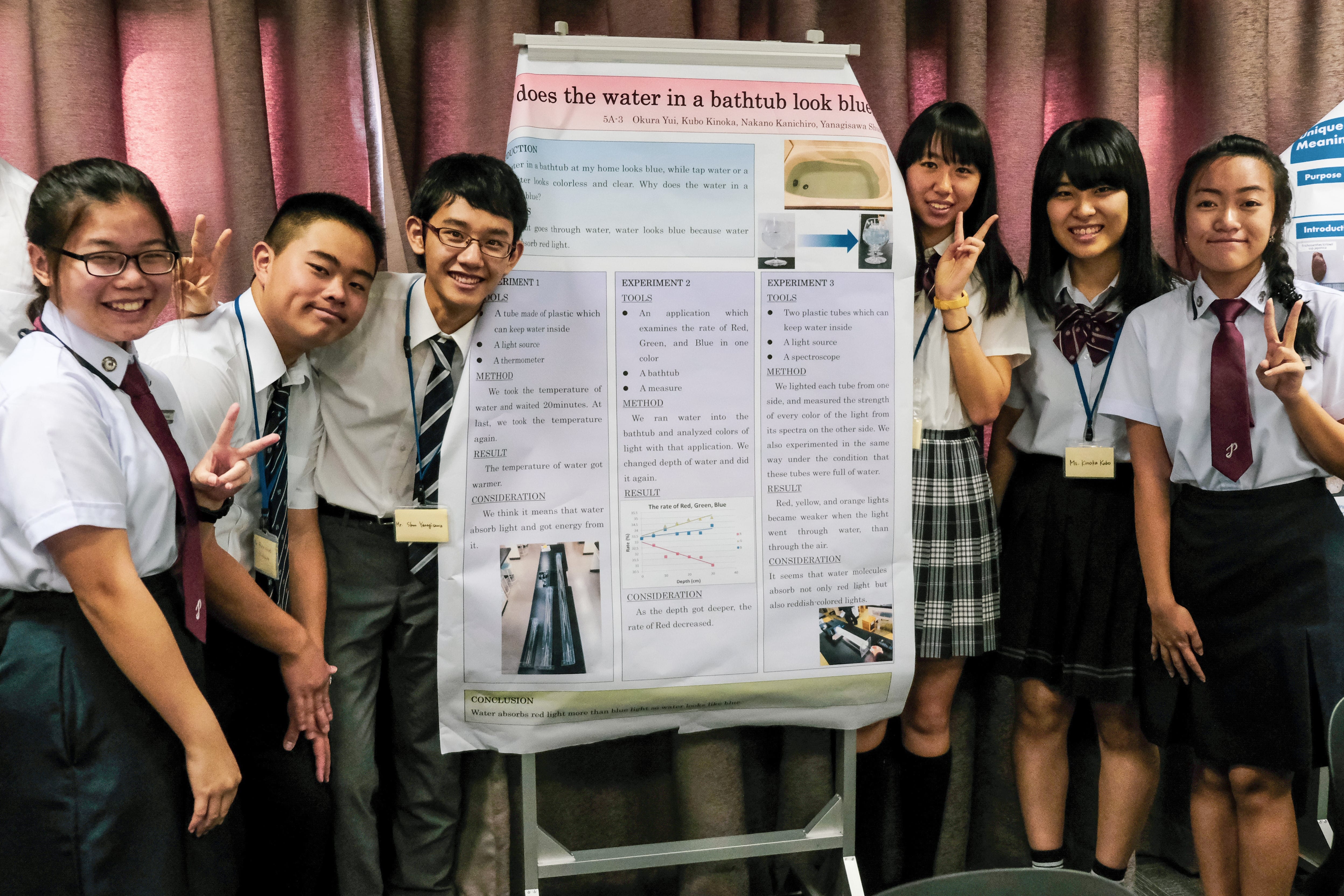 Six students in school uniforms pose beside a science poster titled does the water in a bathtub look blue?